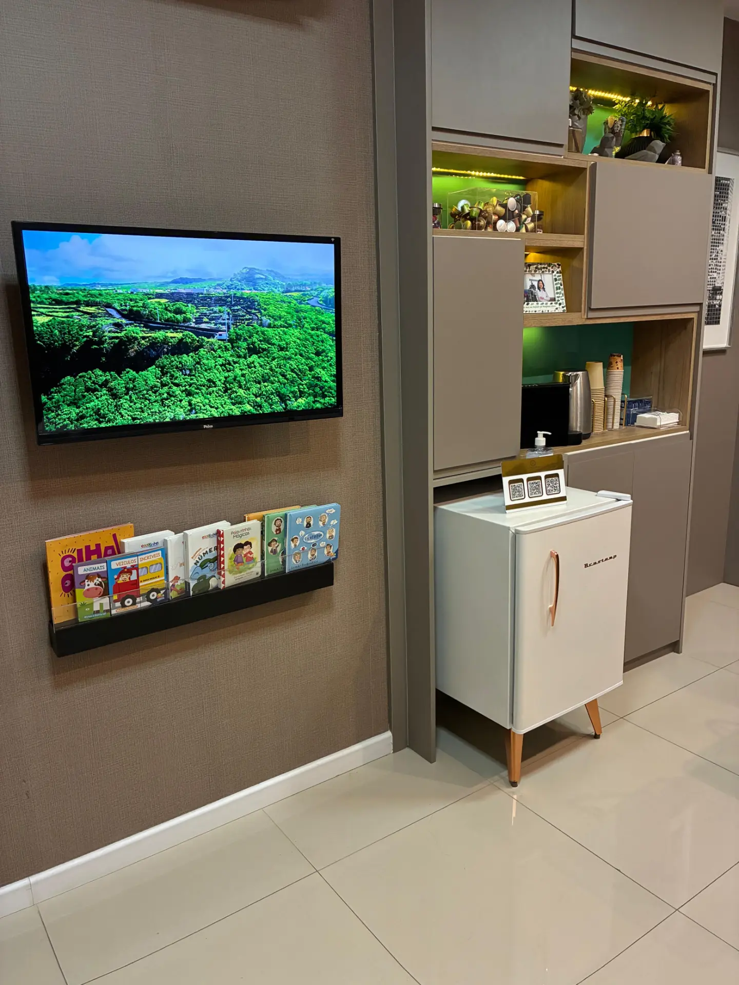Sala de espera com TV, livros infantis e espaço de cafeteria do consultório da Dra. Regina Sakamoto